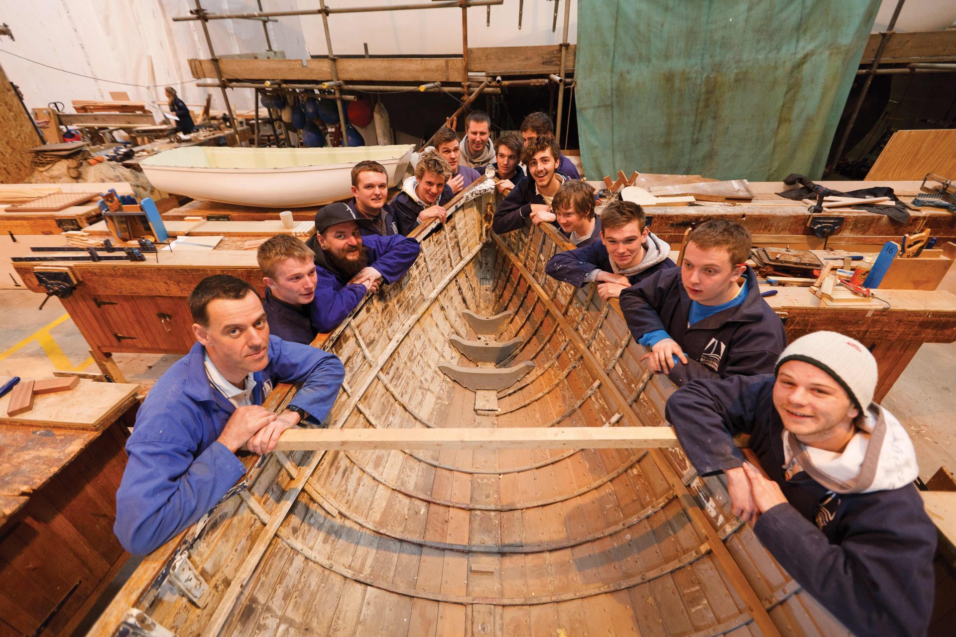 Group of Falmouth Marine School boatbuilding students around a wooden boat they are building